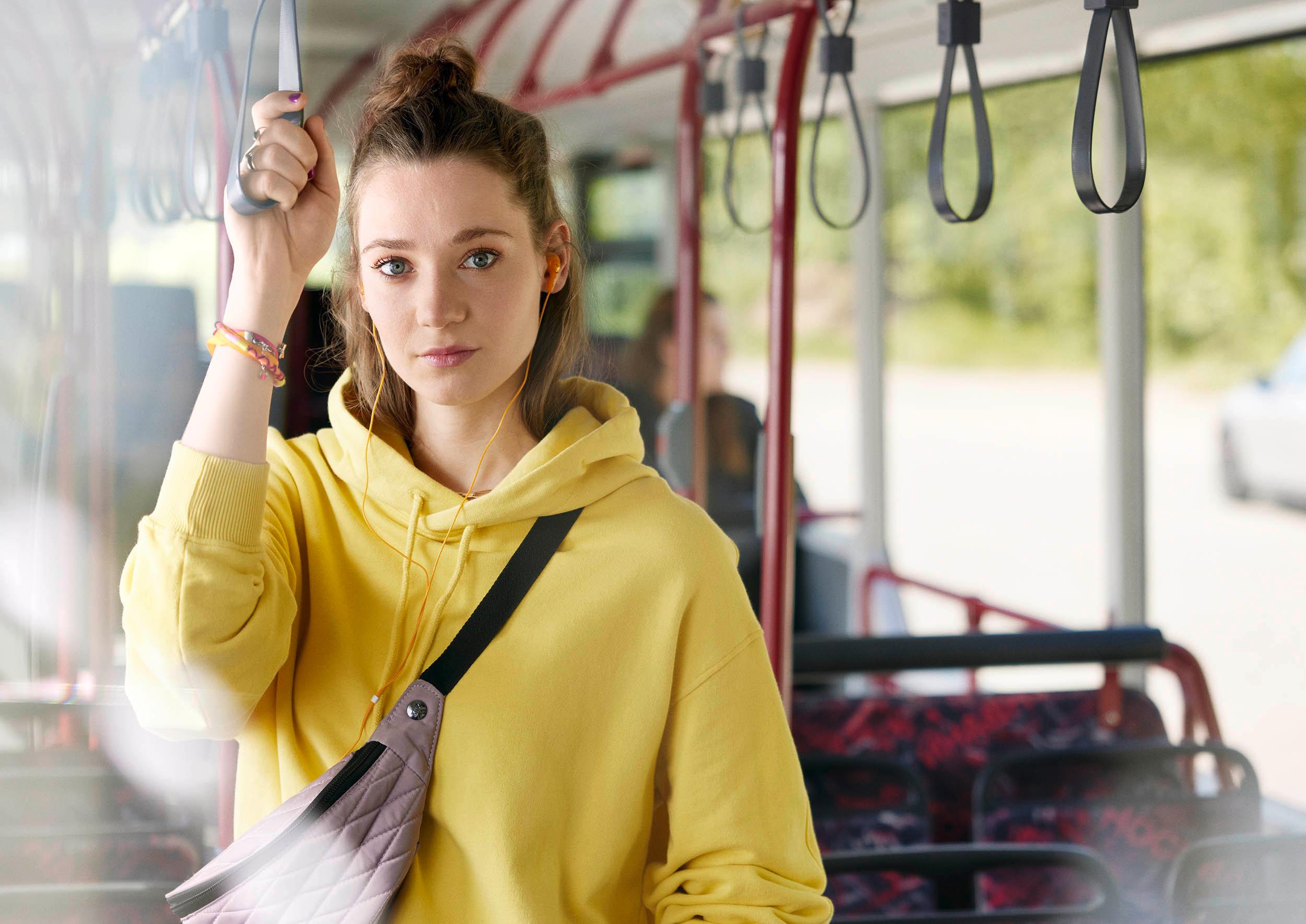 Foto: Junge Frau hält sich im Bus stehend an Haltegriff fest, Frontalaufnahme