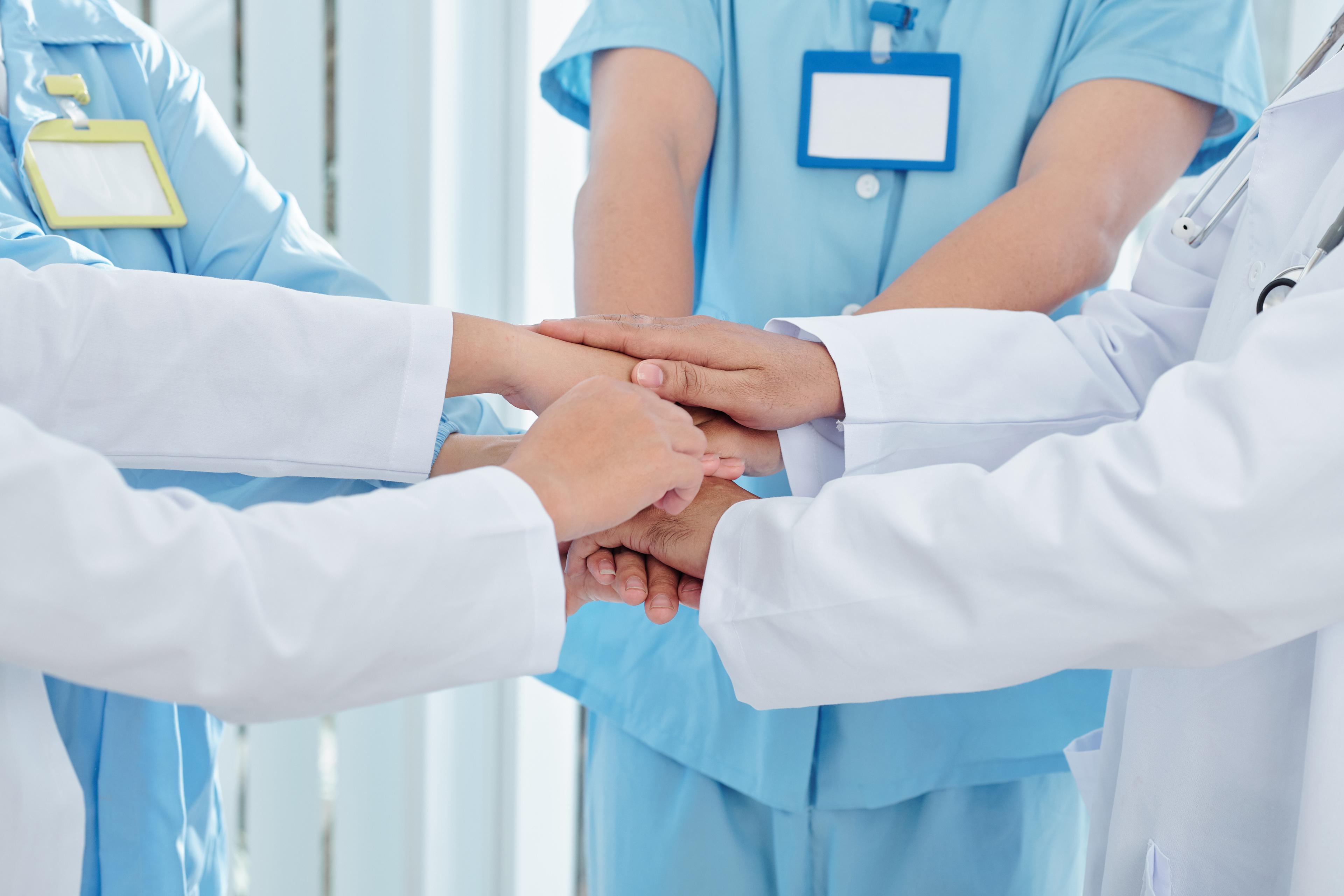 Ärztinnen und Ärzte sowie Pflegerinnen und Pfleger legen die Hände übereinander als Zeichen der Zusammenarbeit